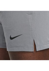 Pantalones cortos deportivos grises con una tela texturizada, presentando un logo negro de Nike en el lado izquierdo y una pequeña abertura lateral cerca del dobladillo.