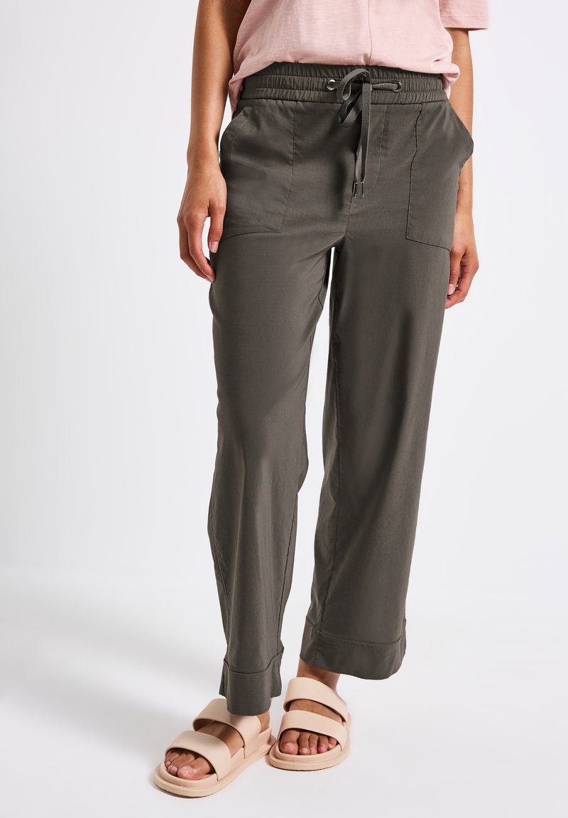 Pantalons gris ajustés avec une taille élastique et des poches latérales. Associé à des sandales à glissière beiges. Tissu lisse et léger.