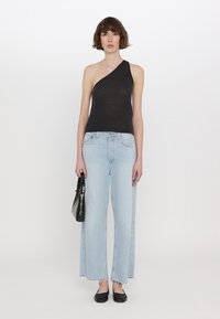 Černý top na jedno rameno, světle modré široké džínsy, zkrácený lem a černá taška. Model má na sobě černé baleríny, minimální vzory, hladká textura.