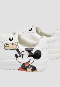 White sneakers with a smooth synthetic upper featuring a large Mickey Mouse graphic on the side, black eyelets, and a textured sole.
