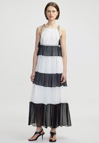 Schwarz-weißer, gestufter Maxikleid aus transparentem Stoff, mit geflochtenen Trägern und Quastenakzenten. Fließende Silhouette mit Rüschenschichten.