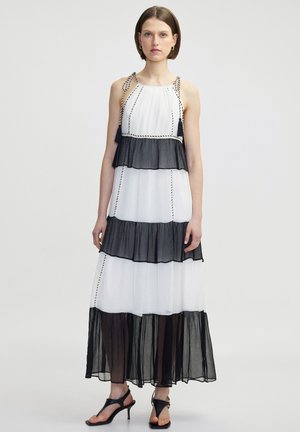 Robe maxi à volants en noir et blanc avec tissu transparent, dotée de bretelles tressées et d'accents à pompons. Silhouette fluide avec des couches froncées.