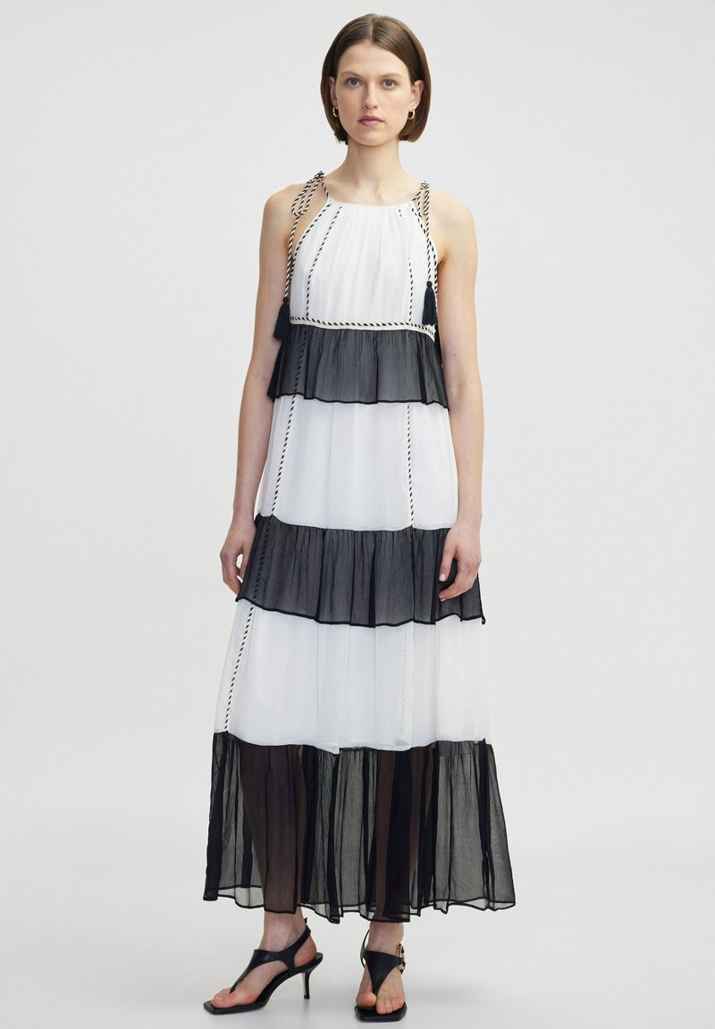 Schwarz-weißer, gestufter Maxikleid aus transparentem Stoff, mit geflochtenen Trägern und Quastenakzenten. Fließende Silhouette mit Rüschenschichten.