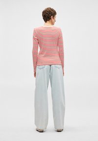 Κόκκινη και λευκή ριγωτή μπλούζα με μακριά μανίκια, συνδυασμένη με ανοιχτόχρωμο τζιν παντελόνι σε φαρδιά γραμμή, που διαθέτει πίσω τσέπες και χαλαρή εφαρμογή.