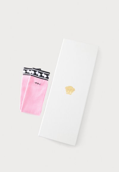 Chaussettes côtelées roses avec poignets à motifs noirs et blancs et texte "Versace", à côté d’une boîte blanche avec un logo Méduse doré.