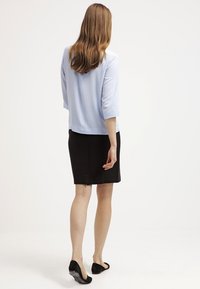 Blusa azzurro chiaro a tre quarti abbinata a una gonna nera al ginocchio. Tessuto morbido con un design semplice e pulito, senza motivi visibili.