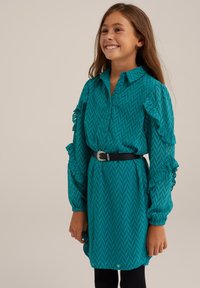 Rochie teal cu un model în zigzag, cu decupaj în față cu nasturi, mâneci volănaș și o curea neagră. Rochia are un material texturat și o margine curbată.