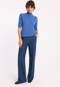 Niebieski sweter z krótkim rękawem w stylu golfu, w połączeniu z ciemnoniebieskimi spodniami dżinsowymi z wysokim stanem, charakteryzującymi się wydłużonymi nogawkami oraz kontrastowym przeszyciem.