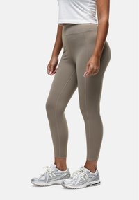 Beige high-waisted leggings van rekbaar materiaal, met platte naden en een aansluitend ontwerp. Gecombineerd met zilveren sport sneakers.