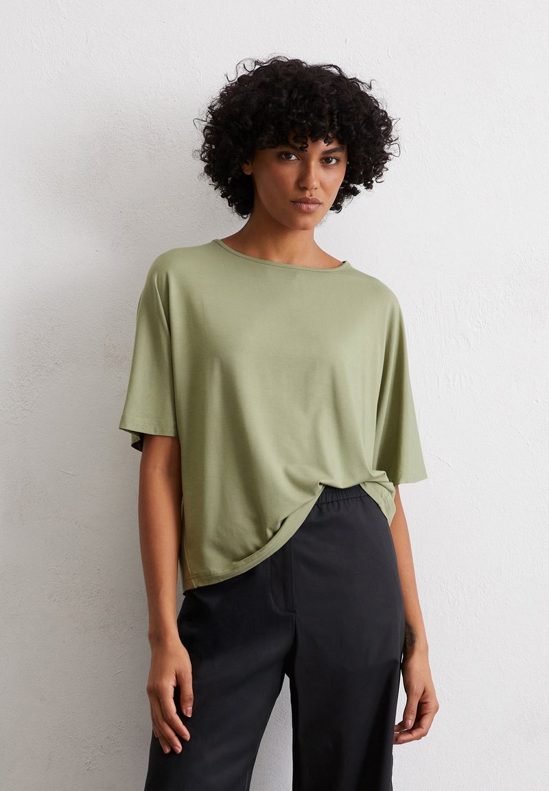 Licht olijfgroene t-shirt met korte mouwen, met een relaxte pasvorm en een afgeronde zoom, gecombineerd met losse zwarte broek. Zachte stofstructuur.