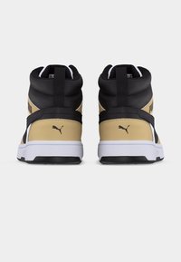 Ζευγάρι αθλητικά παπούτσια υψηλού γλιστρήματος σε μπεζ, μαύρο και λευκό, με θέα από πίσω, που δείχνουν το λογότυπο Puma στις φτέρνες και επενδεδυμένους γιακάδες.