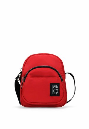 Bolso bandolera de nylon rojo con correa ajustable, forma redondeada, bolsillo con cremallera en la parte frontal y parche de logo negro. Textura suave y diseño minimalista.