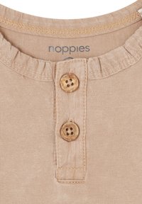 Beige stoffen top met een ronde halslijn, voorzien van drie houten knopen en gerepte stiksels bij de hals. Merkenlabel zichtbaar.