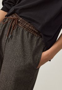 Herringbone patterned pants in gray with a brown elastic waistband and drawstring. Smooth texture. Black top partially visible.