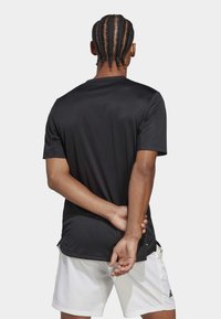 Camiseta deportiva negra de mangas cortas con textura suave, presenta un cuello redondo y sutiles acentos de logo, combinada con pantalones cortos blancos.