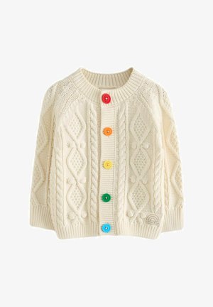 Biela pletená cardigan s textúrovanými vzormi a farebnými gombíkmi (červené, žlté, oranžové, zelené, modré), kombinovaná s kvetinovou sukňou.