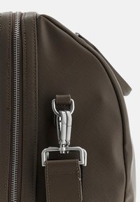 Braune, strukturierte Stofftasche mit einem silbernen Reißverschluss, einem Metallhaken und einem Befestigungsriemen. Verfügt über eine strukturierte Form und ein strapazierfähiges Material.