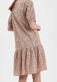 Světlě hnědress s vyšívanými balónkovými rukávy, otevřeným krajkovým vzorem, strukturovanou tkaninou a rozšířeným volánkovým lemem.