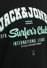 Sort T-shirt med store hvide og mintgrønne tekster. Teksten inkluderer "Jack & Jones," "Surfer's Club," og "International League." Enkel design.