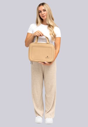 Bolso rectangular beige hecho de material suave, con un bolsillo frontal, asas dobles y un logo en el lateral.