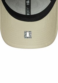 Tan Kappe mit schwarzem Schirm, aus strukturiertem Stoff. Zentrale Logopatch ist rechteckig und mit einem Muster versehen. Innenausstattung hat eine graue Fütterung.