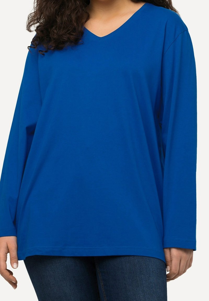 Haut à manches longues en V bleu vif, fabriqué en tissu doux. Présente une coupe décontractée avec des coutures visibles le long de l'ourlet et des manches.