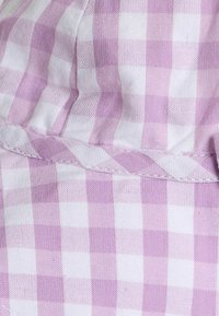 Detailný záber na ružovú a bielu kockovanú látku s viditeľným stehom a prehnutým švom.
