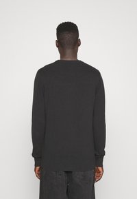 Černý svetr s dlouhým rukávem s žebrovanou texturou, kulatým výstřihem a přiléhavými manžetami, doplněný tmavými kalhotami. Minimalistický design bez viditelných log.