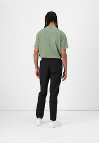 Grüne Baumwoll-T-Shirt mit rundem Ausschnitt, kombiniert mit schwarzen, dehnbaren, schmal zulaufenden Hosen und weißen Turnschuhen. Schlichte Textur, ohne Muster.