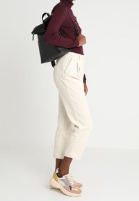 Černý kožený batoh s přední klopou, krémové žebrované kalhoty a vícebarevné tenisky v růžové, šedé a žluté barvě.