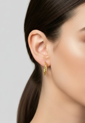 Boucles d'oreilles en or en forme de créole avec un design torsadé, mettant en valeur une surface lisse et une finition polie. Portées à l'oreille gauche.