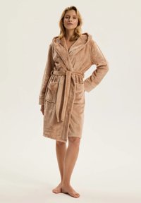 Beżowy miękki szlafrok z polaru z paskiem w talii, kapturem i dwiema przednimi kieszeniami; charakteryzuje się puszystą teksturą i długością do kolan.