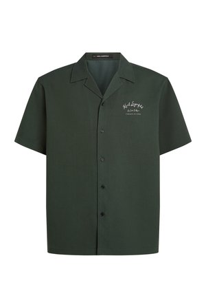 Chemise à manches courtes, vert foncé, en tissu lisse. Elle présente un col, une patte de boutonnage et un texte brodé sur le côté gauche.