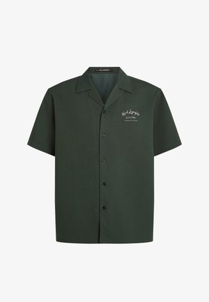 Temno zelena srajca s kratkimi rokavi iz gladkega blaga. Ima ovratnik, sprednje gumbe in vezen napis na levi strani.