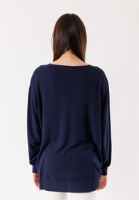 Pullover blu navy, morbido e leggero, con maniche lunghe, polsini a coste e scollatura ampia. Tessuto a maglia soffice, con schiena più lunga e una leggera curvatura.