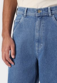 Light blue denim jeans feature a straight cut, a button closure, and classic five-pocket design. The fabric shows a subtle texture.