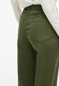 Pantalones verdes de tiro alto, hechos de algodón, que presentan una textura suave, dos bolsillos traseros y un cierre de botón con trabillas para cinturón.
