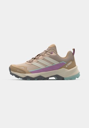 Chaussure d'extérieur marron clair avec une tige en maille, accents violets et verts, embout renforcé et semelle extérieure en caoutchouc texturé pour la traction.
