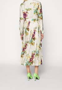 Květnaté šaty s dlouhými rukávy a sklady, s světlým pozadím a živými fialovými a modrými květinami. Nosené s zelenými lodičkami na vysokém podpatku.