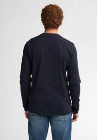 Camicia a maniche lunghe blu navy in cotone, con collo rotondo, vestibilità aderente e texture morbida. Indossata con jeans azzurri chiari.