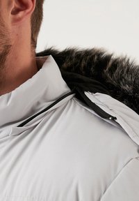 Balta āra jaka ar augstu apkakli, ar melnu vilnas kapuci, sānu rāvējslēdzēja kabatu un gludu auduma tekstūru.