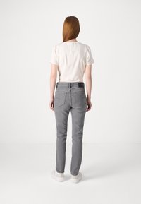 Jeans gris de corte ajustado, con bolsillos traseros y una cintura cosida. Combinados con una blusa blanca de manga corta.
