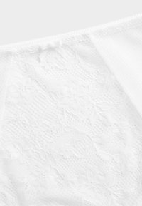 Weißes Spitzenoberteil mit floralen Mustern, einem strukturierten Stoff mit feinem Netz und einem zarten Schleifendetail am Ausschnitt.