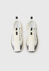 White and dark navy athletic shoes feature a textured mesh upper, lace closure, embossed accents, and a cushioned sole. Black pull tab at rear.