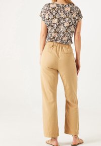 Květinový černý top s krátkými rukávy je spárován s širokými kalhotami s elastickým pasem v světle béžové barvě. Model stojí naboso a ukazuje uvolněný střih.