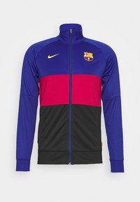 Zip-up jacket in blue, red, and black fabric. Features Nike logo and FC Barcelona crest. Smooth texture, stands with high collar.