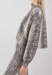 Przycięty, długi rękaw top w wzór węża, z wysokim kołnierzem i luźnym krojem. Wykonany z miękkiej tkaniny w neutralnych odcieniach czerni i bieli.