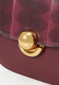 Borsa Furla in bordeaux con finitura a pelle di serpente testurizzata, dotata di una chiusura circolare in metallo dorato lucido e una base in pelle liscia.