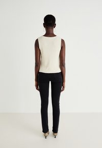 Cream-colored, ribbed knit sleeveless top paired with form-fitting black jeans and beige heeled shoes, viewed from the back.