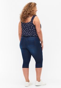 Top sin mangas azul marino con lunares blancos, combinado con unos pantalones capri azul oscuro. Zapatillas y un peinado texturizado y rizado completan el look.